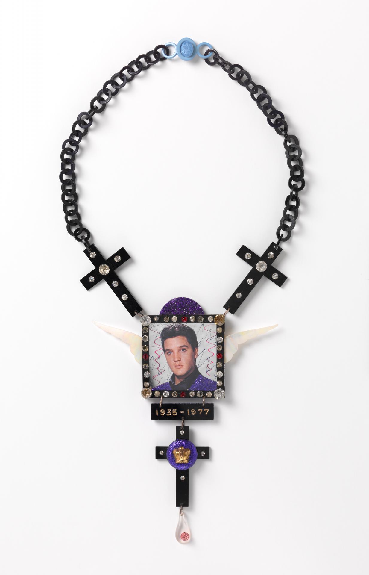 Peter TULLY<br/>
<em>Love me tender, necklace</em> 1977 <!-- (front view) --><br />

plastic, paste, opaque synthetic polymer resin, mirror, enamel paint on colour offset lithograph<br />
38.4 x 14.0 x 1.4 cm<br />
National Gallery of Victoria, Melbourne<br />
Purchased, 1978<br />
D23-1978<br />
© Courtesy of the copyright owner, Merlene Gibson (sister)
<!--15749-->