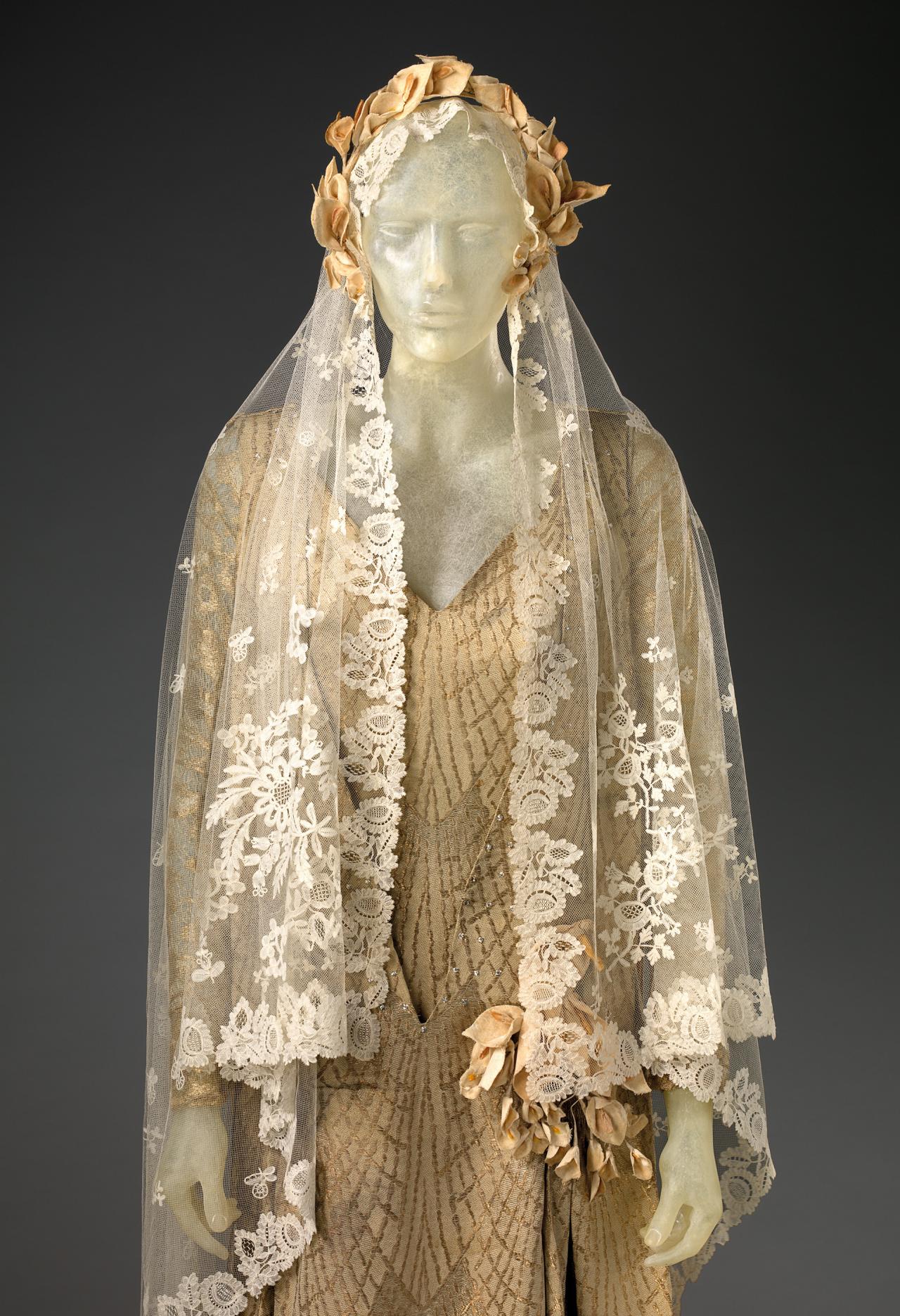 Unknown, Melbourne (dressmaker)<br/>
active 1920s<br/>
C. F. Bally & Co. Ltd., Switzerland (manufacturer)<br/>
1907–99<br/>
<em>Wedding outfit</em> 1925<br/>
silk, metallic thread, glass, cotton (velvet), metal, paper<br/>
(a) 78.0 cm (centre back), 43.5 cm (waist flat) (dress)<br/>
(b) 301.0 cm (length), 69.4 cm (width, hem) (train)<br/>
(c) 186.0 x 165.5 cm (veil)<br/>
(d) 20.0 x 19.0 x 3.0 cm (head wreath)<br/>
(e) 21.3 x 18.0 x 2.0 cm (headpiece)<br/>
National Gallery of Victoria, Melbourne<br/>
Gift of Maurice and Janet Mead, 2010 (2010.511.a-g)<br/>