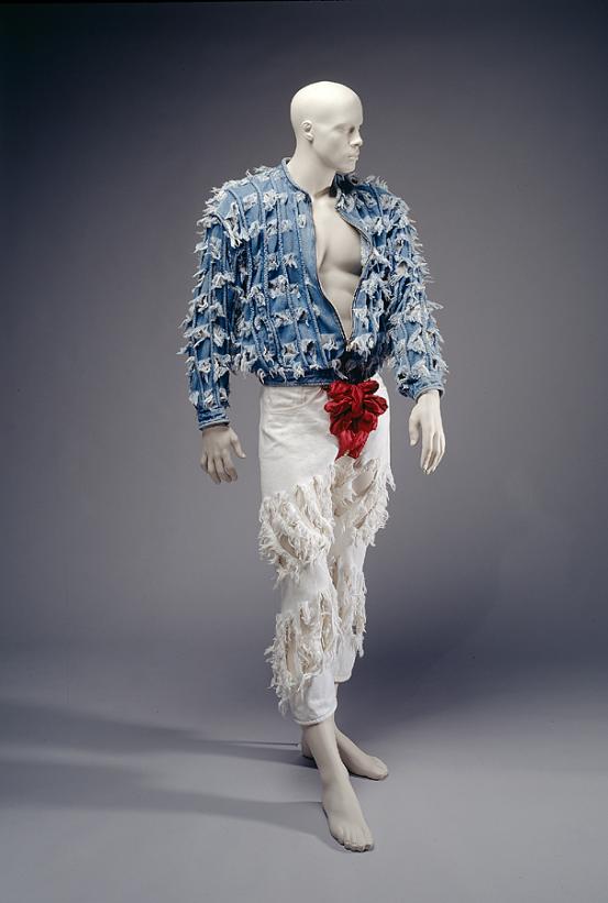 VIVIENNE WESTWOOD, London (fashion house)<br />
 Vivienne WESTWOOD (designer)<br/>
<em>Outfit</em> 1990 {Cut and Slash collection, spring-summer 1991} <!-- (full view) --><br />

cotton, polyester (satin), metal (buttons)<br />
(a) 62.5 cm (centre back) 55.0 cm (sleeve length) (jacket) (b) 93.4 cm (outer leg) 41.2 cm (waist, flat) (jeans) (c) 27.0 x 17.0 cm (codpiece)<br />
National Gallery of Victoria, Melbourne<br />
Purchased, 1995<br />
1995.15.a-c<br />

<!--55984--><br/><a class="col-link block" href="/explore/collection/work/55984"><strong>Collection page <i class="fa fa-angle-right"></i></strong></a>